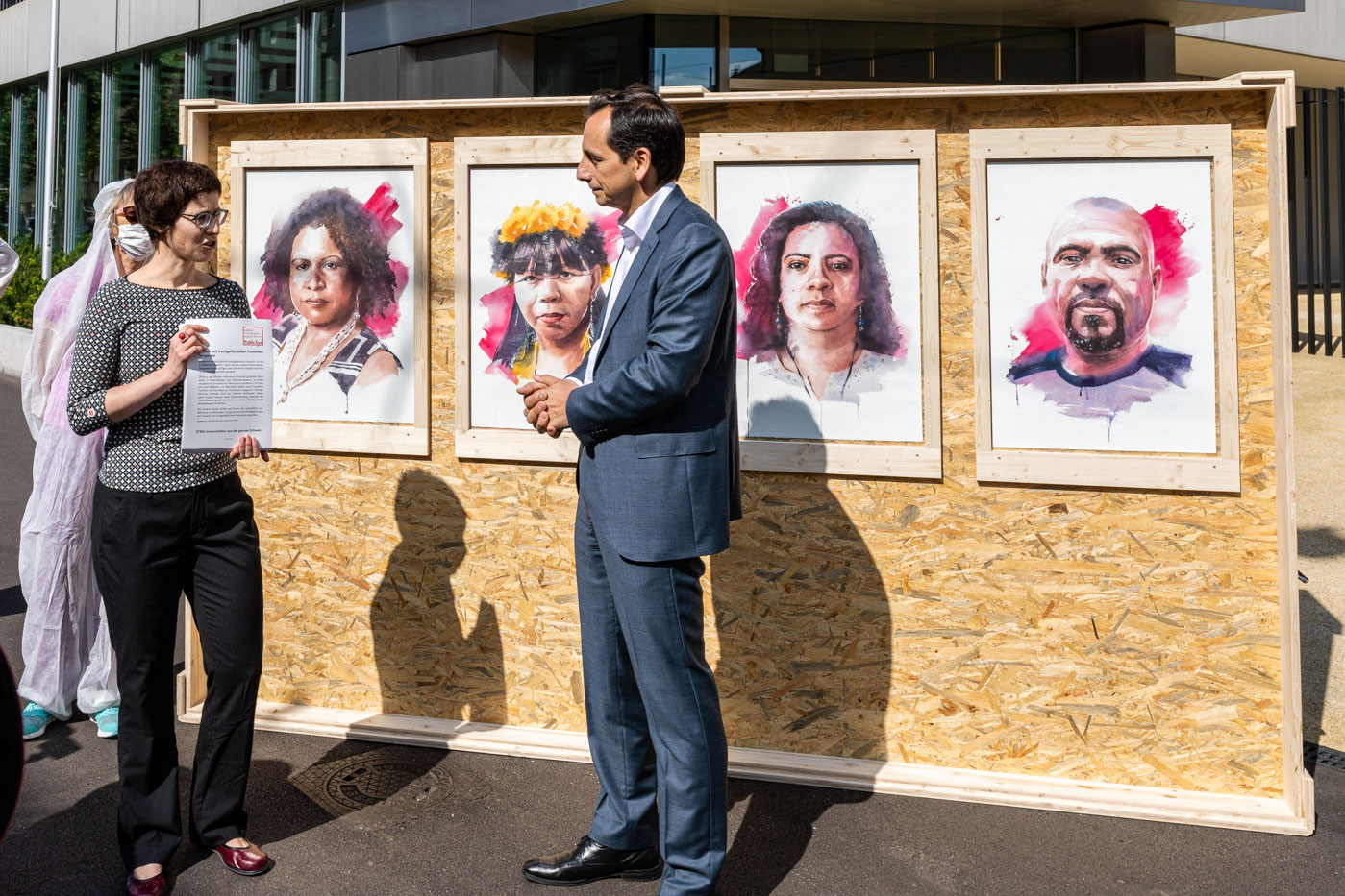 Public Eye remet près de 38'000 signatures au directeur de Syngenta Suisse, Roman Mazzotta, pour demander à la firme de mettre un terme à la production et à la vente de pesticides extrêmement dangereux. En arrière-plan, des portraits de militant-e-s brésilien-ne-s, peints à l’eau contaminée aux pesticides.